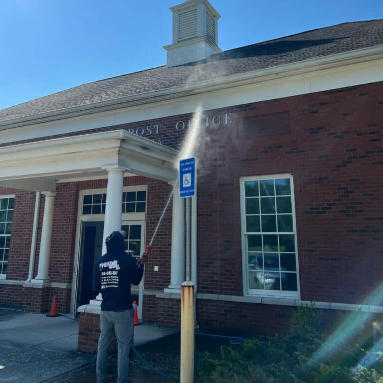 Person using soft washing to clean exterior brick walls of post office in suwanee georgia